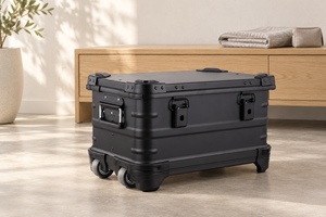 Black aluminum rolling case in a warm neutral storage setting; lifestyle scene, props not included