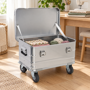 Open silver aluminum rolling trunk beside a sewing table with example fabrics and yarn; contents not included